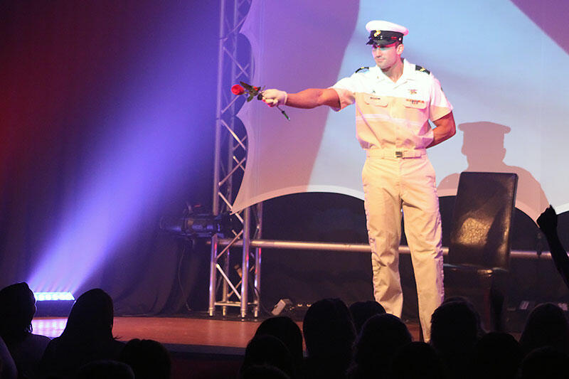 Thomas Rooney on stage performing as a Naval Officer Headline Performer and author Thomas (Tom) Rooney of in his Naval officer costume holding a rose and pointing at the audience